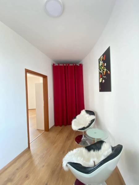 ☎️ 0918197701   Na predaj  elegantný 3 izbový byt priamo v centre Duna - Izba v 3-izbovom byte s podlahou s dreveným dekorom, červenými závesmi a kreslami.