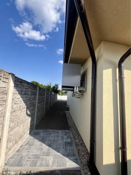 Jedinečný 5 izbový dom na predaj v TOP lokalite-GARDEN TOWN - Rodinný dom v GARDENTOWN, Dunajská Streda s chodníkom vedľa múru a modrou oblohou.