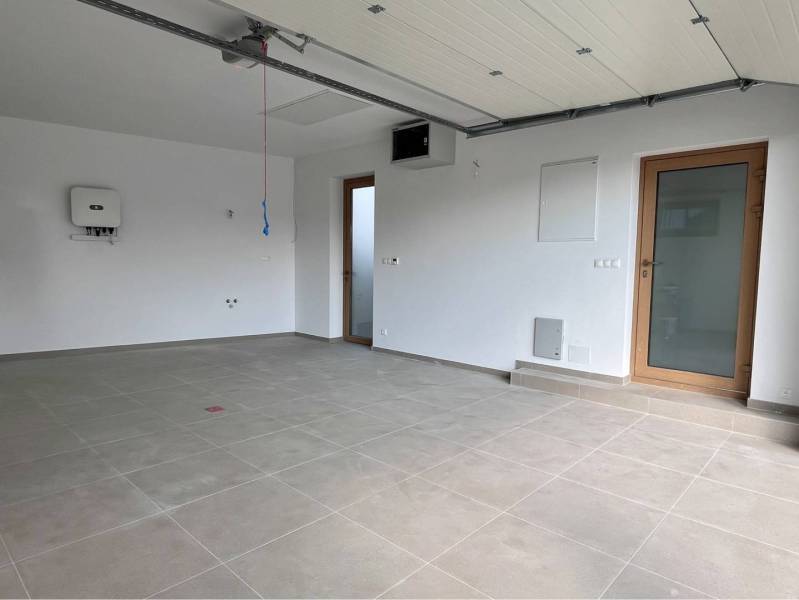 Jedinečný 5 izbový dom na predaj v TOP lokalite-GARDEN TOWN - Garáž v rodinnom dome s dlažbou a garážovou bránou, obsahuje biele steny.