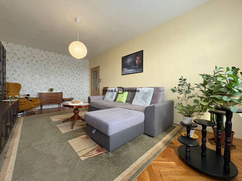 Na predaj: CENTRUM veľký 3 izb.byt + BALKON + ŠATNIK - Opis obývacej izby, sivý gauč, rastliny, vzorovaná tapeta, koberce, atmosféra a 3-izbový byt.