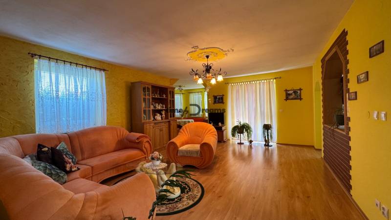 NA PREDAJ 4 izbový rodinný dom Nitrianske Hrnčiarovce - Obývacia izba v rodinnom dome s oranžovými sedačkami a podlahou s dreveným dekorom.