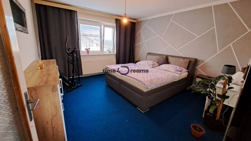 NA PREDAJ 6 izbový rodinný dom v obci Hrušovany  - Spálňa v rodinnom dome s modrým kobercom, posteľou a rotopedom.