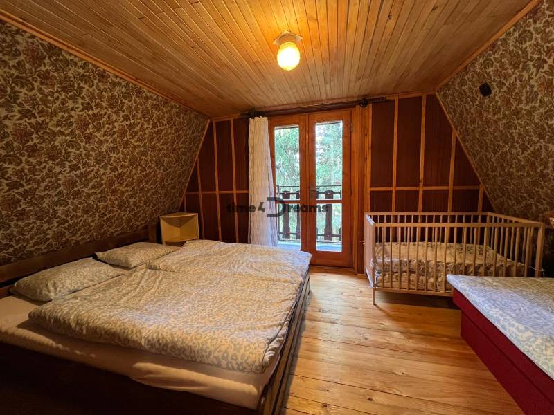 NA PREDAJ Chata na Duchonke-Prašice - Interiér chaty s posteľou, detskou postieľkou a podlahou s dreveným dekorom.