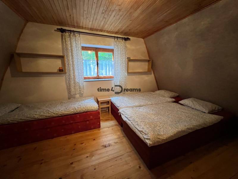 NA PREDAJ Chata na Duchonke-Prašice - Chata s tromi lôžkami, dekor dreva, poličky a okno s bielymi závesmi.