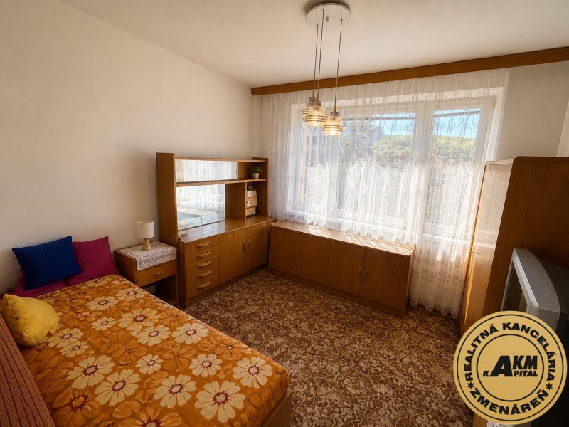  3 izbový byt s balkónom 75m2 Zvolen - Západ - Izba s posteľou a skriňou v 3-izbovom byte s kvetinovým kobercom.