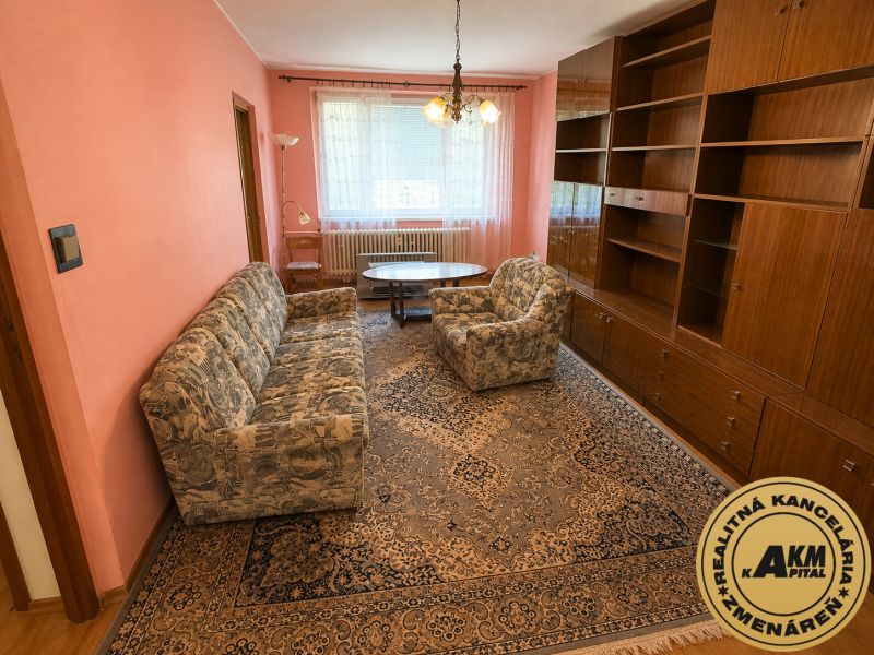  3 izbový byt s balkónom 75m2 Zvolen - Západ - Obývačka v 3-izbovom byte s ružovými stenami, vzorovaným kobercom a drevenými skrinkami.