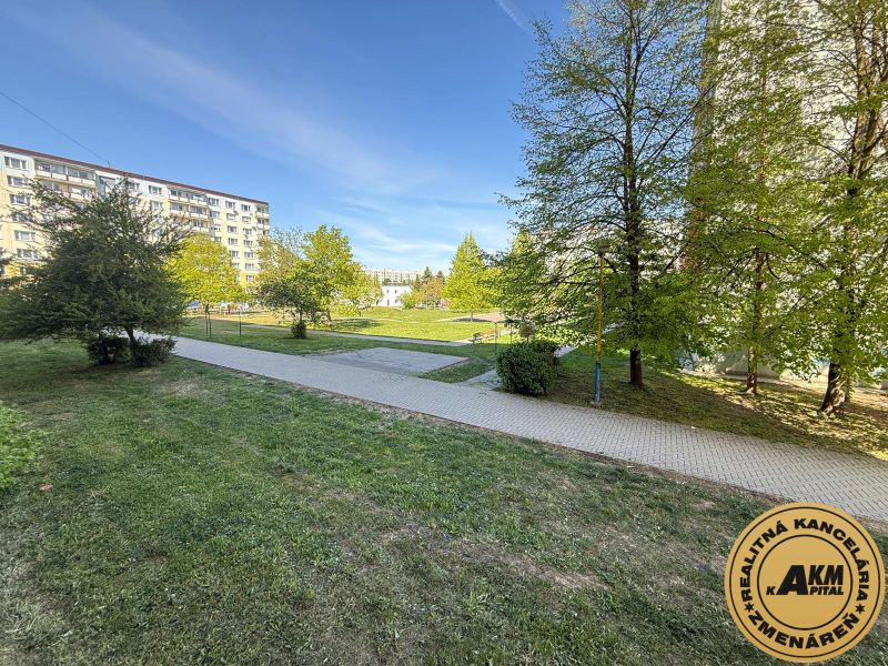  3 izbový byt s balkónom 75m2 Zvolen - Západ - Trávnatá plocha s chodníkom a bytovkami na Tulskej ulici vo Zvolene.