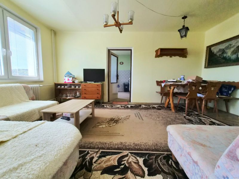 3 izbový byt 77m2 s balkónom Trenčín - Kubrá  - Obývacia izba v 3-izbovom byte s kobercami, sedačkou a stolom vedľa kuchyne.