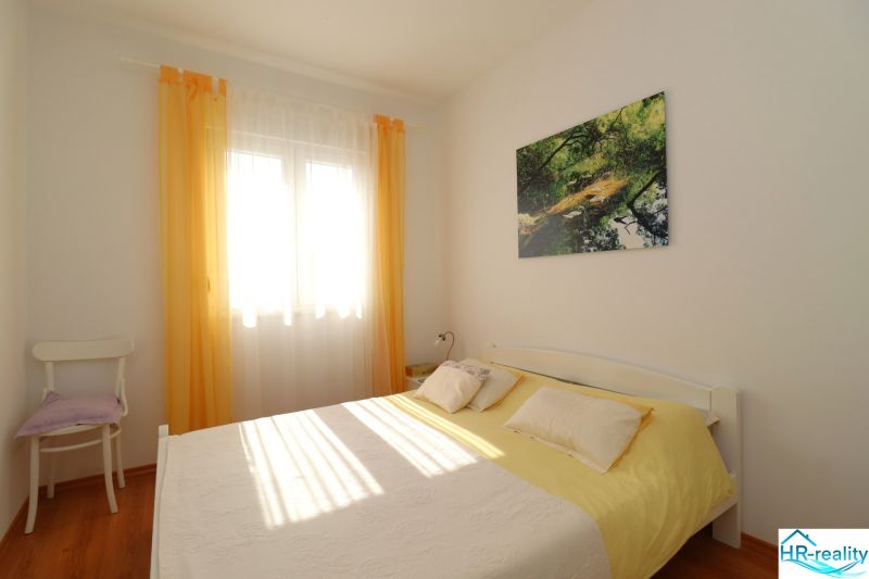 Chorvátsko, Vodice - zariadený bungalov, výhľad na more - Spálňa v rodinnom dome s posteľou, kreslom a podlahou s dreveným dekorom.