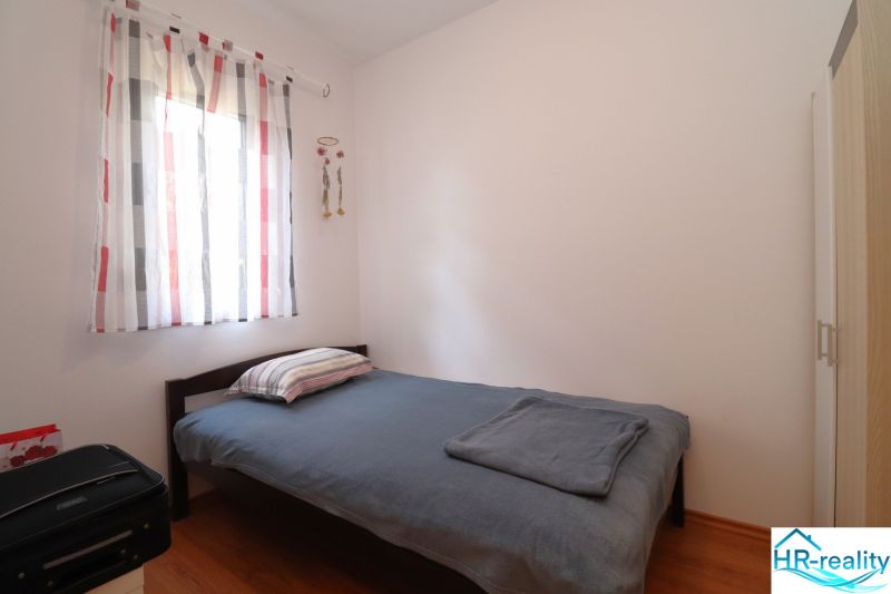 Chorvátsko, Vodice - zariadený bungalov, výhľad na more - Jednoduchá spálňa s posteľou, podlahou s dreveným dekorom a svetlými závesmi.