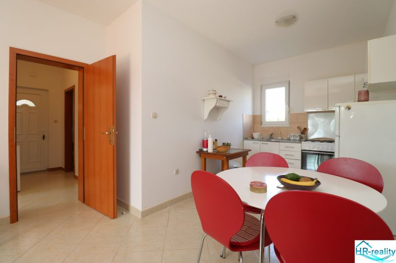 Chorvátsko, Vodice - zariadený bungalov, výhľad na more - Jedáleň so stolom a červenými stoličkami v rodinnom dome, svetlá dlažba.