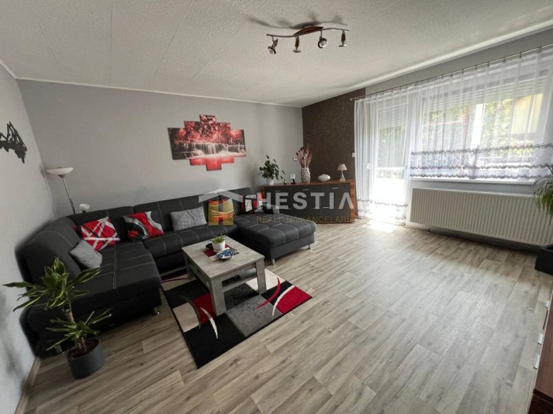 NOVINKA Priestranný 3-izbový byt (99 m²) s pozemkom, terasou, 2 balkón - Priestranná obývačka v 3-izbovom byte s podlahou s dreveným dekorom a pohodlnou sedacou súpravou.