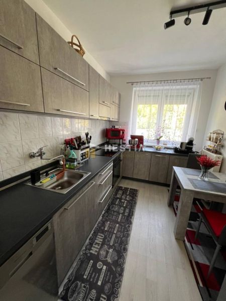 NOVINKA Priestranný 3-izbový byt (99 m²) s pozemkom, terasou, 2 balkón - Kuchyňa s kuchynskou linkou, stolom a podlahou s dreveným dekorom v 3-izbovom byte.