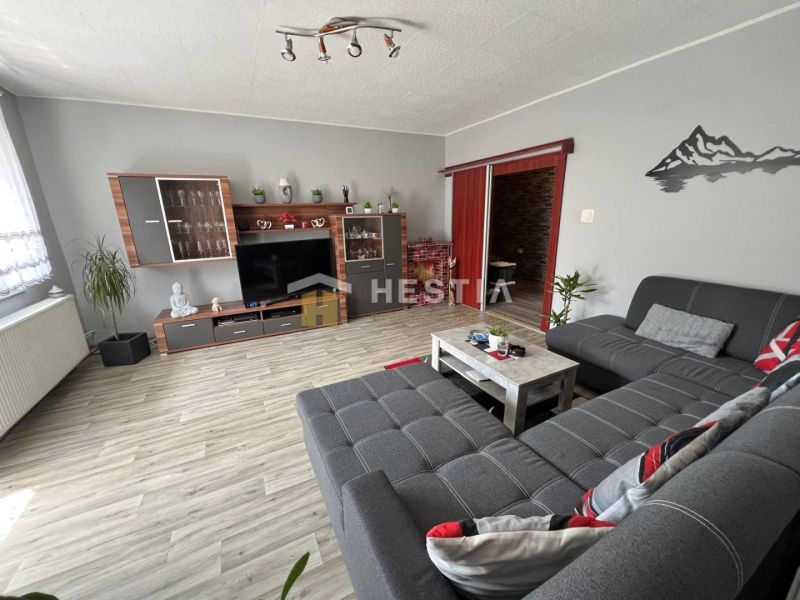 NOVINKA Priestranný 3-izbový byt (99 m²) s pozemkom, terasou, 2 balkón - Obývacia izba v 3-izbovom byte s gaučom a podlahou s dreveným dekorom.
