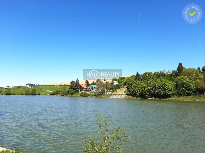 Predaj, záhradný pozemok   1050 m2 Hubina, neďaleko ... - Vodná plocha a domy v okolí záhrad v Hubine, obklopené zeleňou a modrou oblohou.