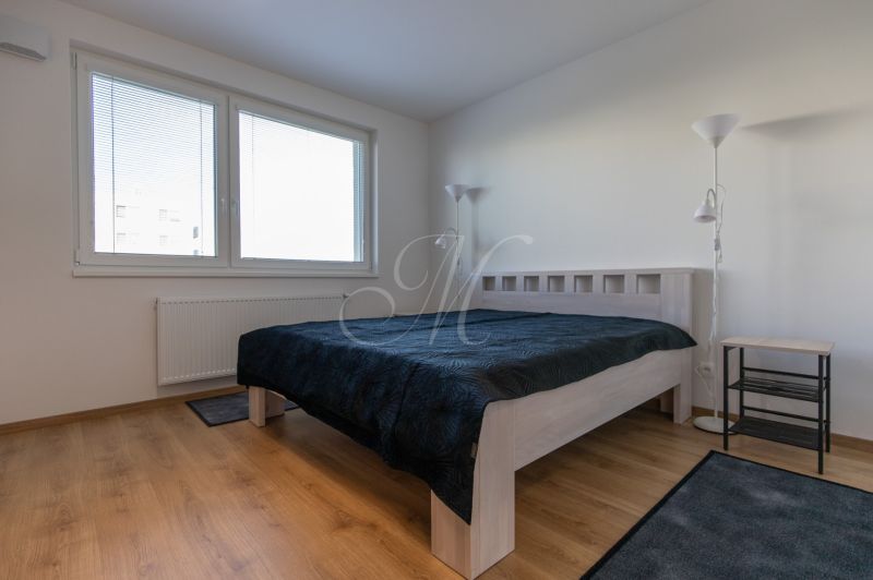 Moderný 2-izbový byt s balkónom, Ovocné sady - Spálňa v 2-izbovom byte s posteľou, lampou a podlahou s dreveným dekorom.