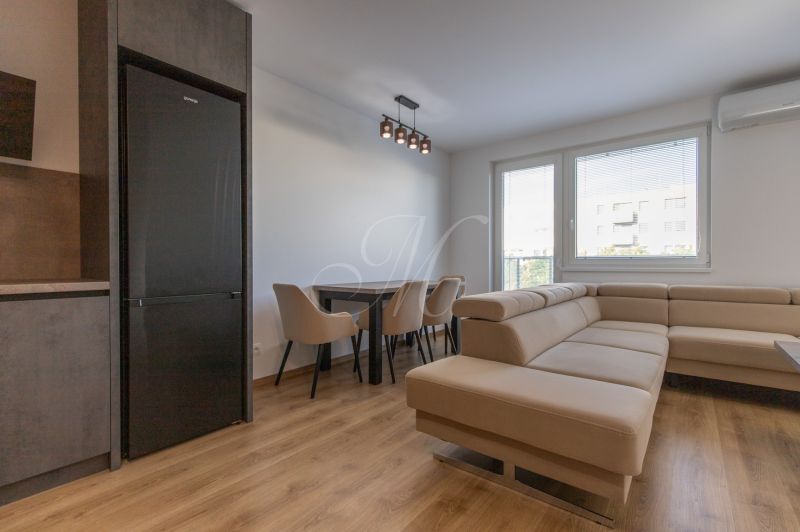 Moderný 2-izbový byt s balkónom, Ovocné sady - Obývačka s koženou sedačkou, jedálenským stolom a podlahou s dreveným dekorom v 2-izbovom byte.