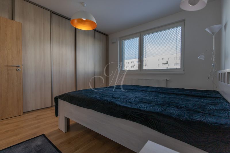 Moderný 2-izbový byt s balkónom, Ovocné sady - Spálňa v 2-izbovom byte s posteľou, vstavanou skriňou a podlahou s dreveným dekorom.