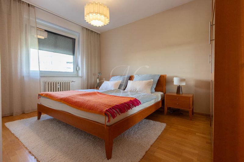 Zariadený 4-izbový byt s balkónmi a parkovaním - Spálňa s manželskou posteľou, nočným stolíkom a podlahou s dreveným dekorom v 4-izbovom byte.
