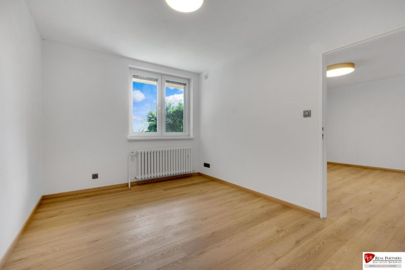,Prenájom moderný 3 izb. byt, Sološnícka ul,124 m2, Karlova Ves - Prázdna izba s podlahou s dreveným dekorom v rodinnom dome, biele steny a okno.
