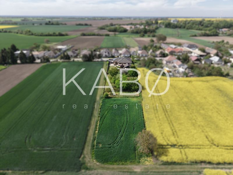 Nadštandardný 5-izbový RD - veľkorysý pozemok - moderné technológie - Rodinný dom na Močenskej ulici v Cabaji-Čápore obklopený zelenými a žltými poľami.