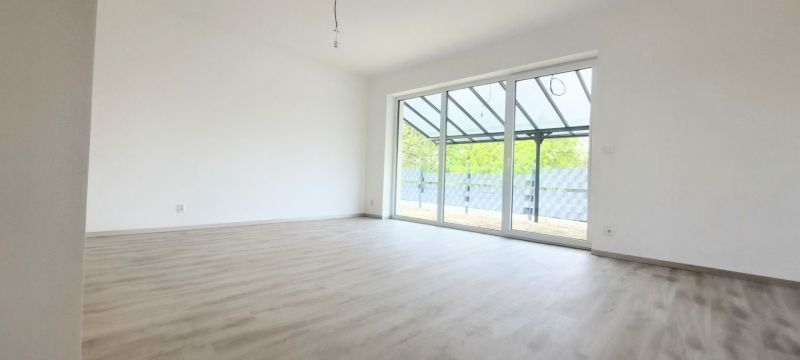 Novostavba pri jazere - 4 izbový rodinný dom v štandarde v obci Selice - Priestranná miestnosť v rodinnom dome s podlahou s dreveným dekorom a veľkým presklením.