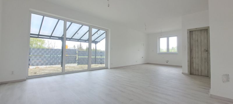 Novostavba pri jazere - 4 izbový rodinný dom v štandarde v obci Selice - Priestranný interiér rodinného domu s veľkými oknami a podlahou s dreveným dekorom.
