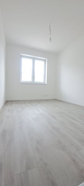 Novostavba pri jazere - 4 izbový rodinný dom v štandarde v obci Selice - Izba s bielymi stenami, podlahou s dreveným dekorom a oknom v rodinnom dome.