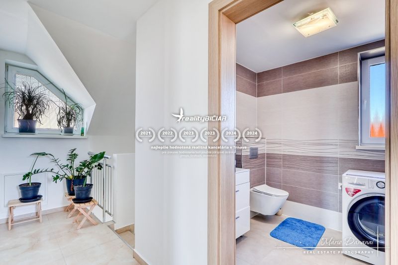REZERVOVANÉ 5-izbový rodinný dom Hrnčiarovce - Kúpeľňa v rodinnom dome s rastlinami, dlažbou a práčkou, svetlé a elegantné prostredie.