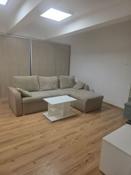 Moderný prenájom na ulici Bakossova za 550 € mesačne - 1-izbový byt s rohovou sedačkou, stolíkom a podlahou s dreveným dekorom.