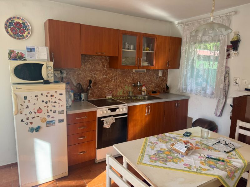 NA PREDAJ celoročná chata – Sekule (Šutrovňa), tiché prostredie - Interiér chaty so staršou kuchynskou linkou, chladničkou a dekoratívnym tanierom na stene.