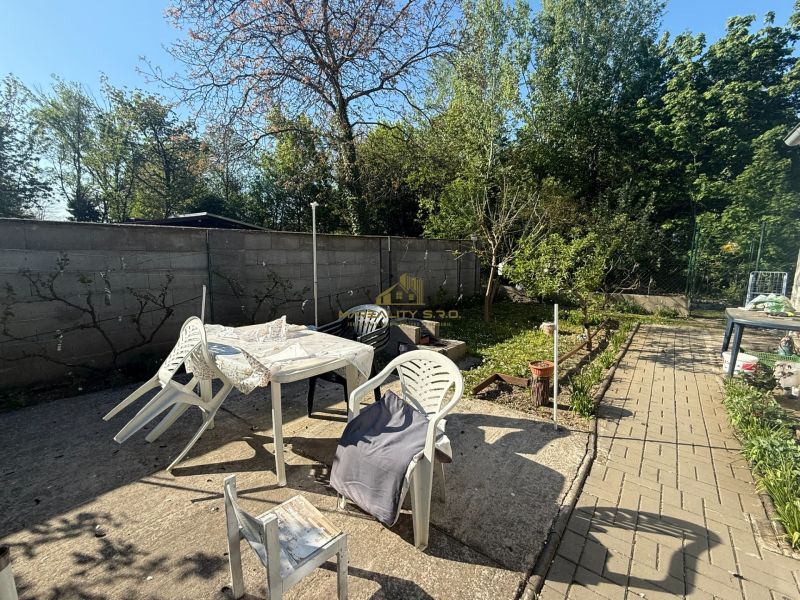 NA PREDAJ celoročná chata – Sekule (Šutrovňa), tiché prostredie - Záhrada chaty v Sekuliach s plastovým nábytkom a stromami po okrajoch.