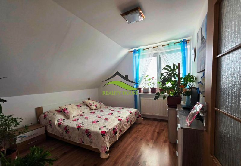 Poschodový rodinný dom v  obci Klokočov okr. Michalovce - Spálňa v rodinnom dome s posteľou, podlahou s dreveným dekorom a izbovými rastlinami.