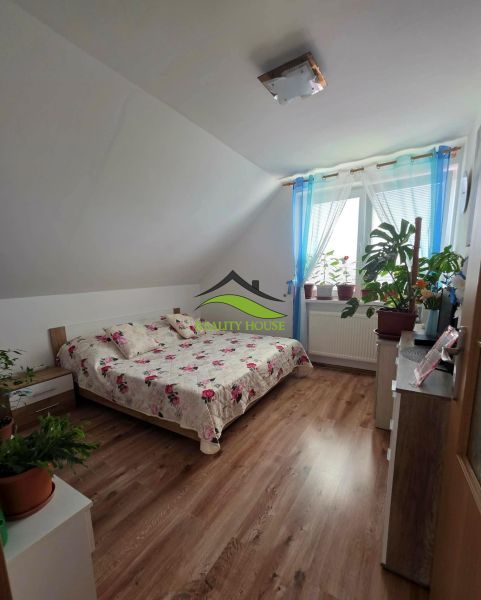 Poschodový rodinný dom v  obci Klokočov okr. Michalovce - Spálňa v rodinnom dome so podlahou s dreveným dekorom a posteľou s kvetinovým prehozom.