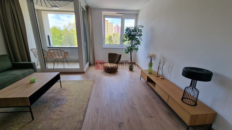 Exkluzívne 2 izbový byt POPRAD Karpatská, s garaž. st., balkón, 58 m2 - Obývacia izba v 2-izbovom byte s podlahou s dreveným dekorom a veľkým oknom.