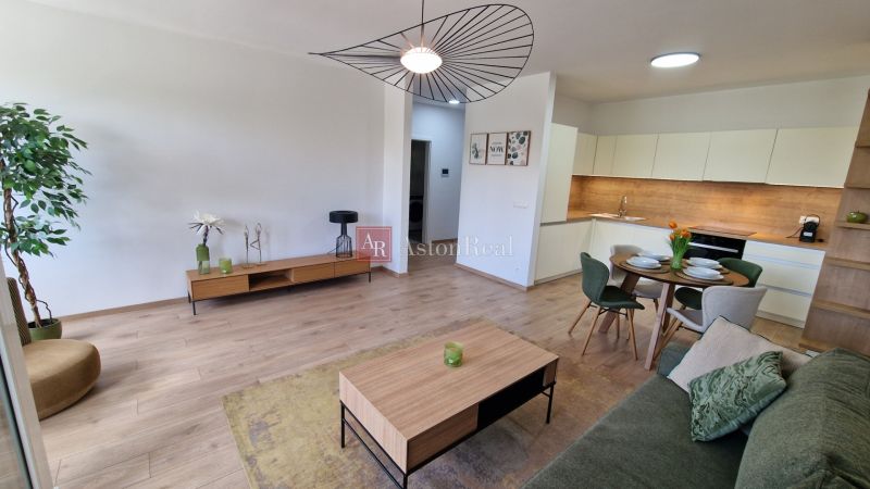 Exkluzívne 2 izbový byt POPRAD Karpatská, s garaž. st., balkón, 58 m2 - Obývacia izba s kuchyňou v 2-izbovom byte, podlaha s dreveným dekorom, elegantný nábytok.