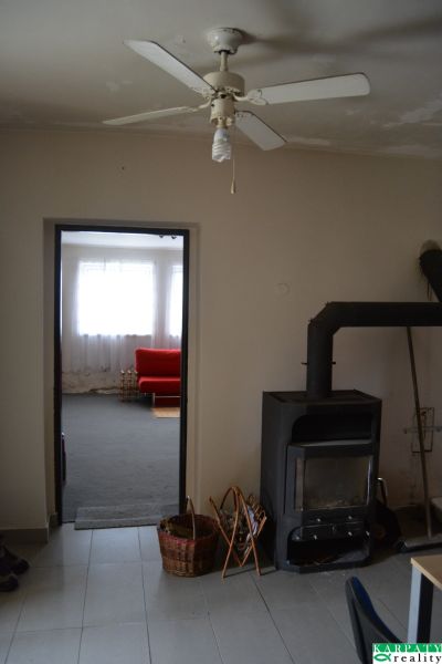 Domček na chalupárčenie s veľkým pozemkom s termál kúpaliskom v obci! - V Rodinnom dome je stropný ventilátor, kachle a červený gauč v pozadí.