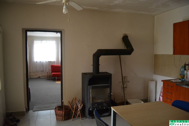 Domček na chalupárčenie s veľkým pozemkom s termál kúpaliskom v obci! - Interiér rodinného domu s krbom, ventilátorom a červenou sedačkou v pozadí.