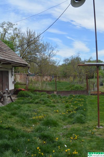Domček na chalupárčenie s veľkým pozemkom s termál kúpaliskom v obci! - Rodinný dom v Horných Salibách s trávnikom a záhradou, okolo ktorého je plot.