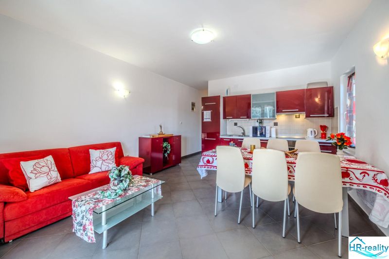 Brač(HR) - Apartmány v 1. rade u mora !!! - Rekreačný apartmán s červenou sedacou súpravou a kuchyňou s jedálenským kútom.