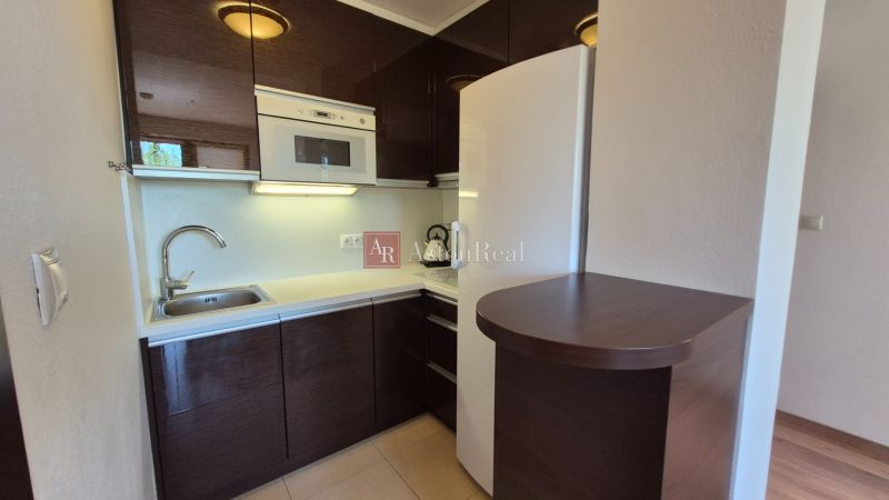 Investičný apartmán Vysoké Tatry - Stará Lesná s balkónom a park.miest - Kuchynský kút v rekreačnom apartmáne s tmavými skrinkami a bielymi spotrebičmi.