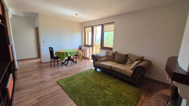 Investičný apartmán Vysoké Tatry - Stará Lesná s balkónom a park.miest - Obývacia izba s pohovkou, jedálenským stolom, policou a podlahou s dreveným dekorom v Rekreačnom apartmáne.
