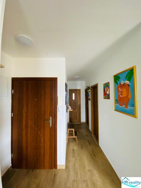 Brač(HR)–Apartmán s výhľadom na more - Chodba rekreačného apartmánu s podlahou s dreveným dekorom a farebnými obrazmi na stenách.