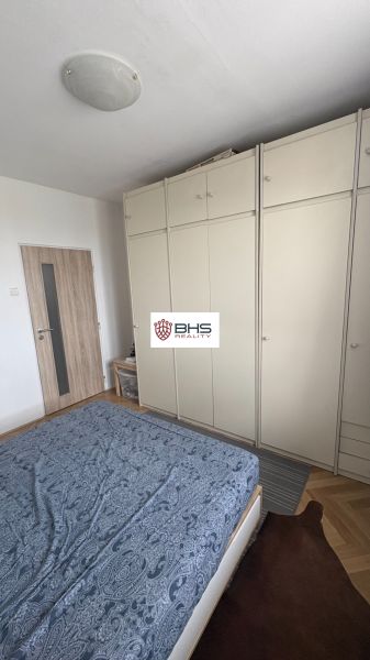 Prenájom 2i-byt s lodžiou s krásnym výhľadom na Račianskej ulici - Spálňa s posteľou, skriňou a podlahou s dreveným dekorom v 2-izbovom byte.