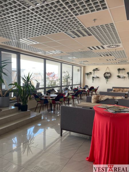 ODSTÚPENIE ZABEHNUTEJ KAVIARNE V CENTRE TRNAVY – TROJIČNÉ NÁMESTIE - Interiér gastro priestorov s kvetmi, farebnými stoličkami a pohovkami na podlahe s dekorom.
