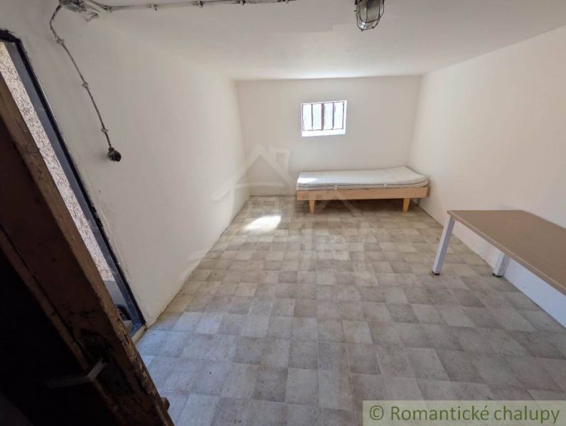 SOBOTIŠTE – VIDIECKY DOM PO ZÁSADNEJ REKONŠTRUKCII ( PRIPRAVENÝ NA DOK - Izba v rodinnom dome s posteľou, stolom a oknom, svetlé steny.