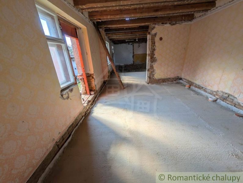 SOBOTIŠTE – VIDIECKY DOM PO ZÁSADNEJ REKONŠTRUKCII ( PRIPRAVENÝ NA DOK - Interiér rodinného domu s odkrytými drevenými stropmi a poškodenými stenami.