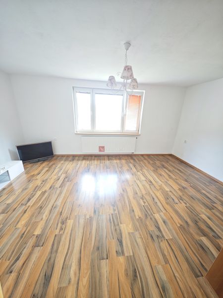 Rezervované: 3 izbový TEHLOVÝ byt 83m2 s loggiou - Uľanka  - Priestranná obývačka s podlahou s dreveným dekorom a veľkým oknom v 3-izbovom byte.