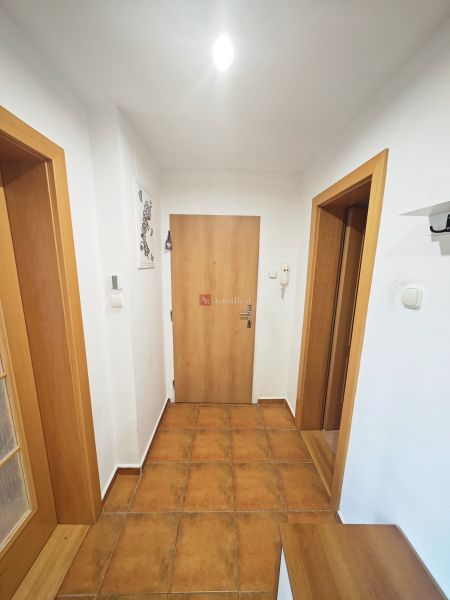 Rezervované: 3 izbový TEHLOVÝ byt 83m2 s loggiou - Uľanka  - Chodba v 3-izbovom byte s keramickou dlažbou, bielymi stenami a drevenými dverami.