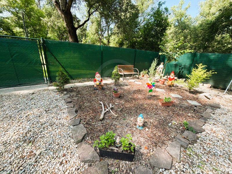 Celoročne obývateľná chata v Gabčíkove na 150 m² pozemku pri Dunaji - Záhrada s trpaslíkmi a lavičkou pri chate v Gabčíkove, obkolesená kameňmi a plotom.